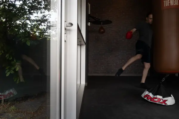 Foto von Mann beim Kickbox Training mit großem Box-Sack und verspiuegelter Scheibe Richtung Garten im Manhattan Club Brunn